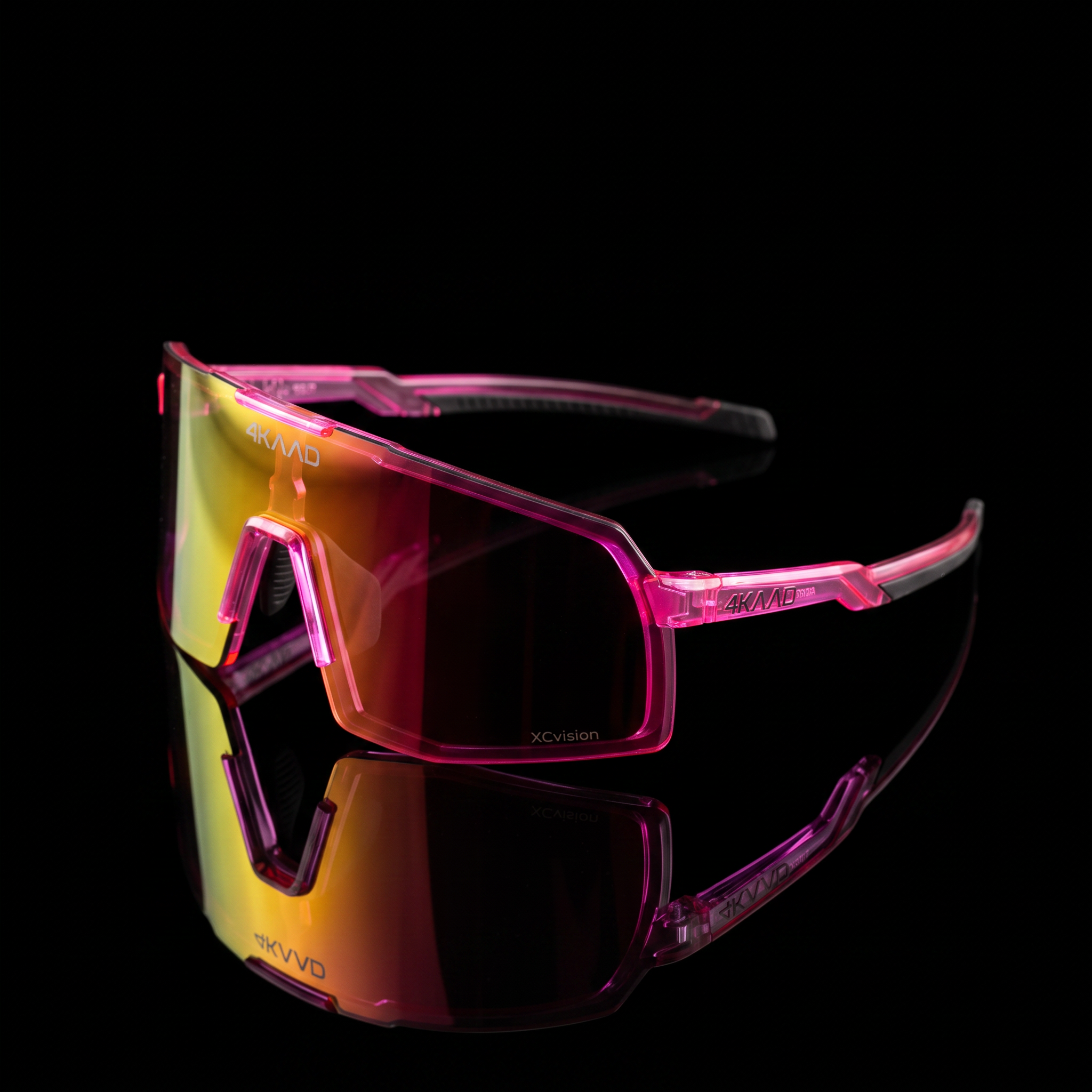 Skvado sports sunglasses with a translucent pink frame and a large shield lens featuring a yellow-to-pink gradient, shown on a reflective black surface against a black background. 4kaad eyewear products for cycling
