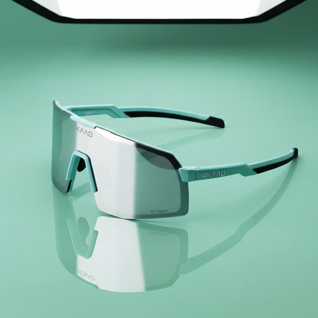 A pair of shield-style sunglasses with a large mirrored lens and turquoise and black arms, photographed on a smooth mint-green surface with a reflection below. The brand name 4KAVUD is visible on the lens and arm.