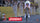 A cyclist in a white and red cycling jersey rides a time trial bicycle down a race street, with a crowd of spectators blurred in the background behind yellow barriers. An Enervit logo is displayed prominently at the bottom of the image.