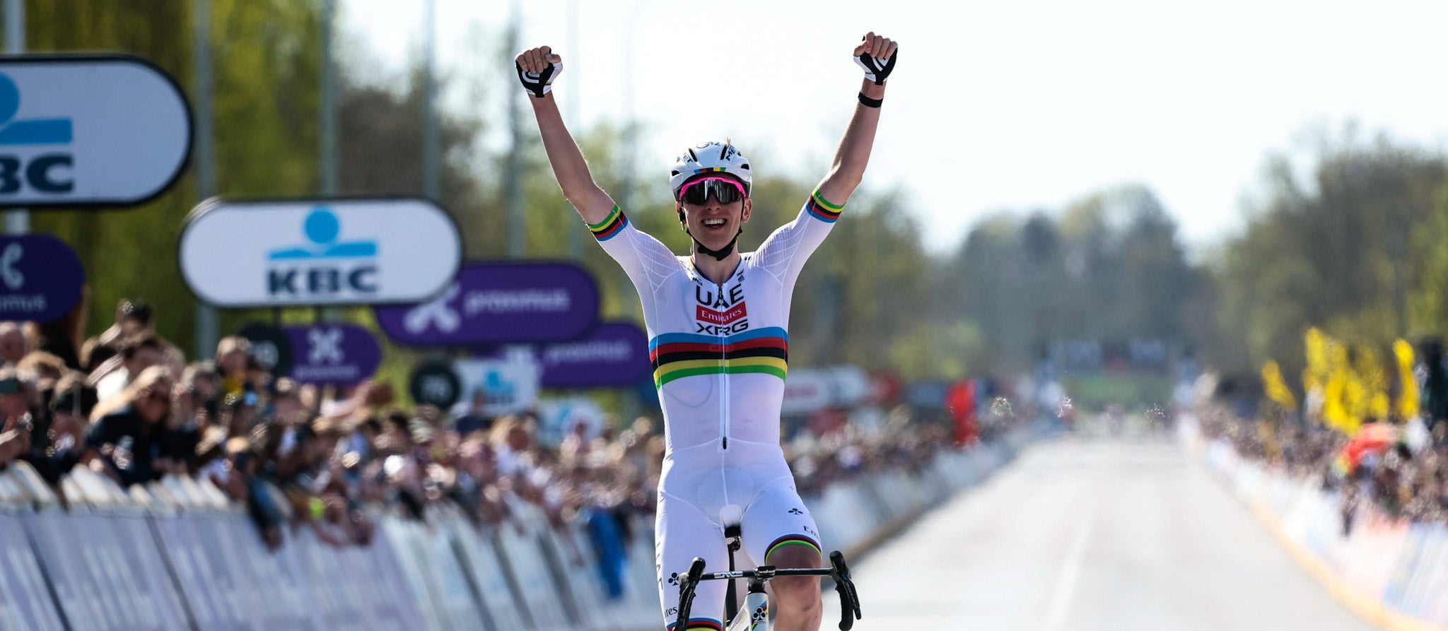 Cyclist in a rainbow jersey celebrating on a race track with spectators and branding in the background. Enervit Finland
