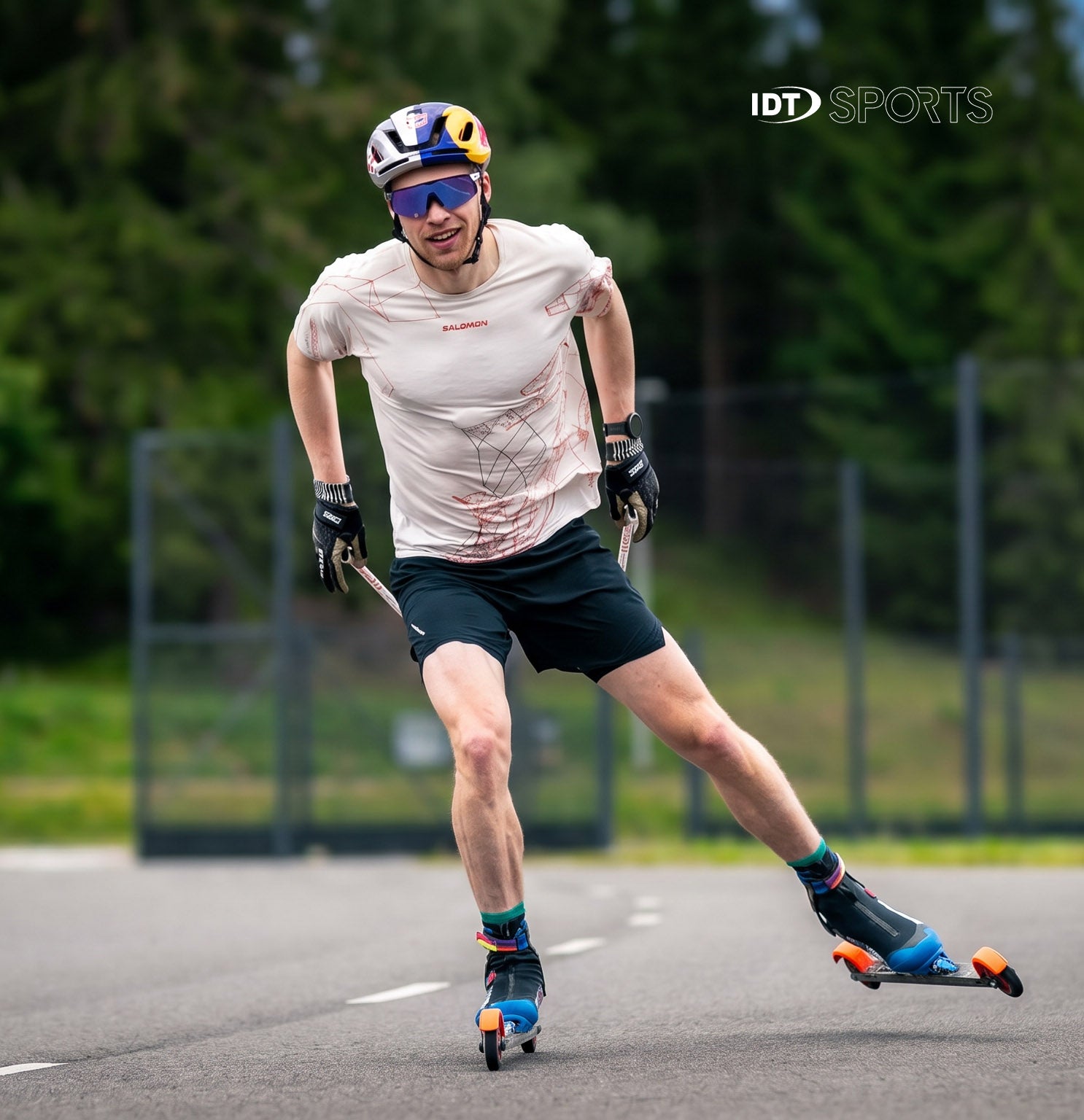 Iivo Niskanen roller skiing on a paved surface with greenery in a green background