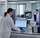 A scientist in a white lab coat and blue gloves uses a computer at a lab bench, with another scientist and laboratory equipment visible in the background. development of fluor free wax maplus brand in Finland