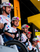 A group of professional cyclists wearing white team jerseys with red and blue checkered patterns, white helmets, and sunglasses, riding bicycles in a bright indoor cycling environment.
