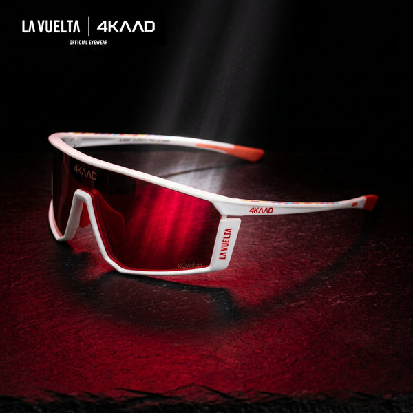 White and red LA VUELTA x 4KAAD sports sunglasses with a red mirrored lens, displayed on a dark textured surface with dramatic red lighting.